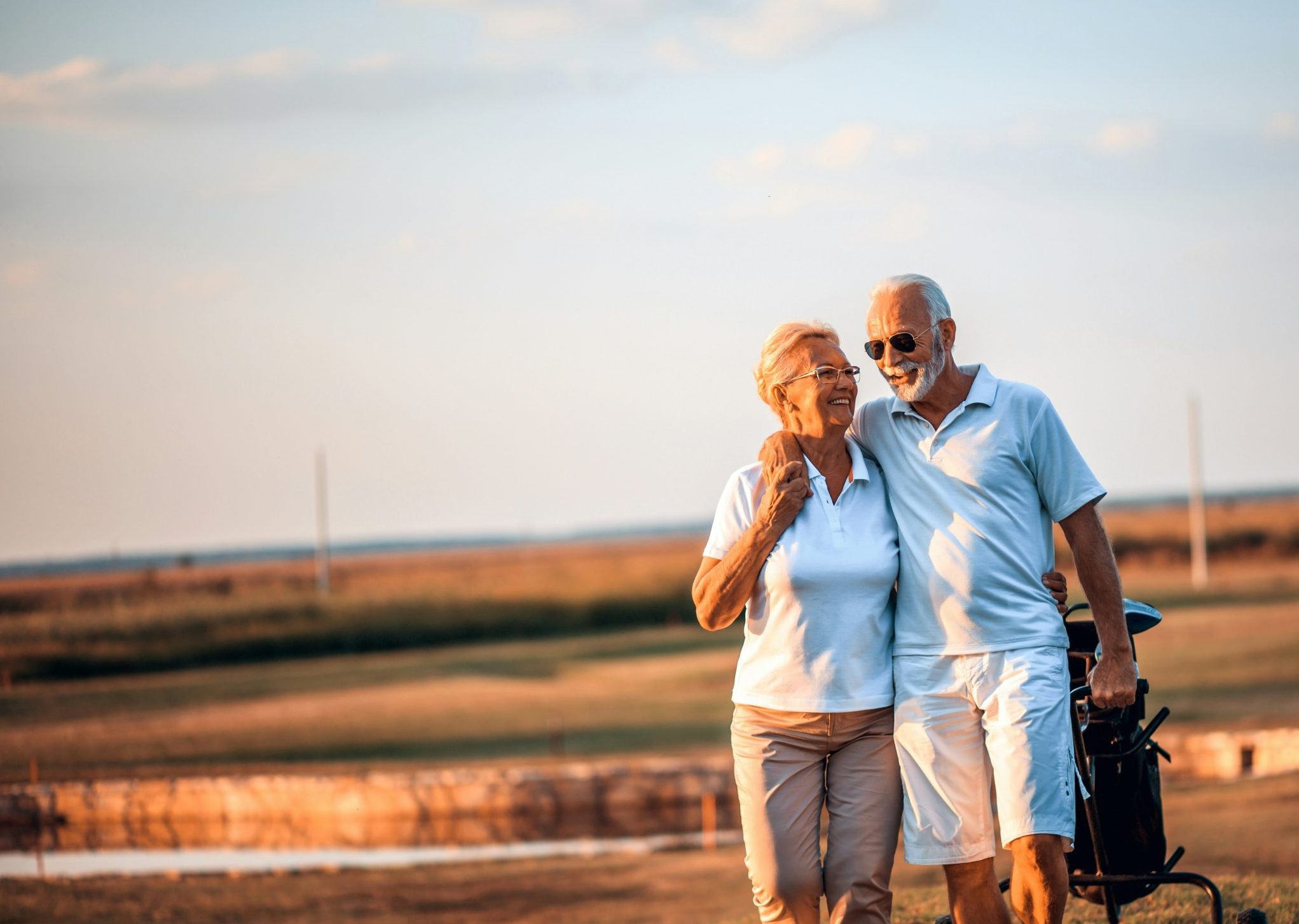 A retired couple walking together on a golf course at sunset